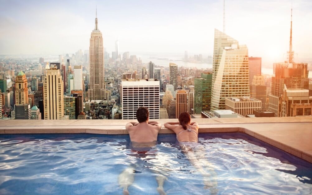 PowerBall Jackpot Gewinner Lifestyle – Paar entspannt im Infinity-Pool mit Blick auf die Skyline von New York City und das Empire State Building bei Sonnenuntergang, Symbol für amerikanischen Traum und Lottoland PowerBall