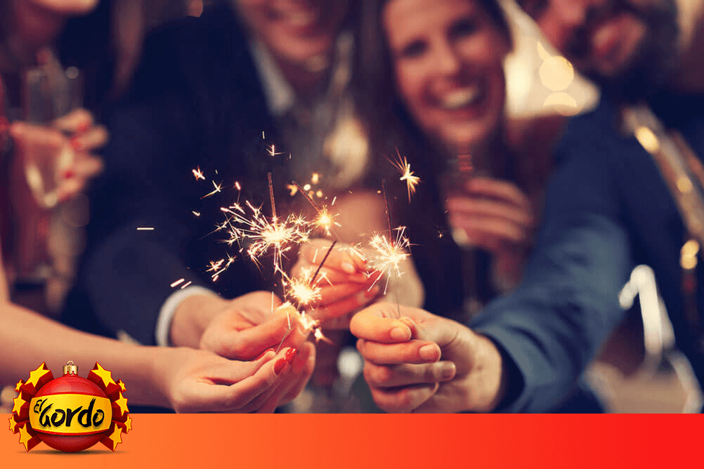 Bild zeigt eine Gruppe fröhlicher Menschen, welche mit Wunderkerzen die El Gordo Weihnachtslotterie feiern.