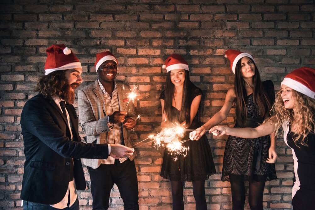 Fünf Freunde mit Weihnachtsmützen feiern mit Wunderkerzen