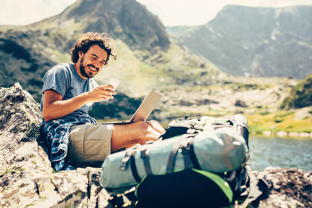 So wirst du digitaler Nomade Ein Mann lächelt während er als digitaler Nomade in einer wunderschönen Bergumgebung arbeitet