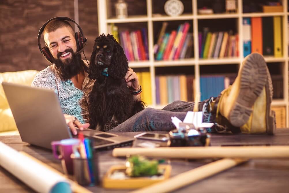 Bärtiger Mann mit Hund spielt lächelnd Lotto online von Zuhause