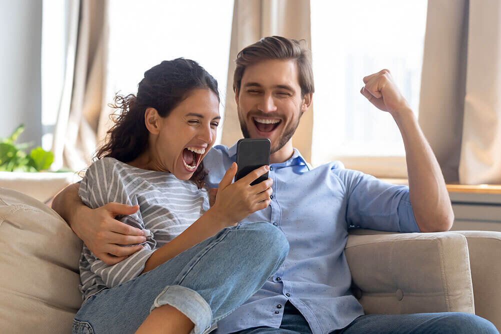 Ein Mann und eine Frau sitzen auf dem Sofa und freuen sich über ihren EuroMillionen-Gewinn