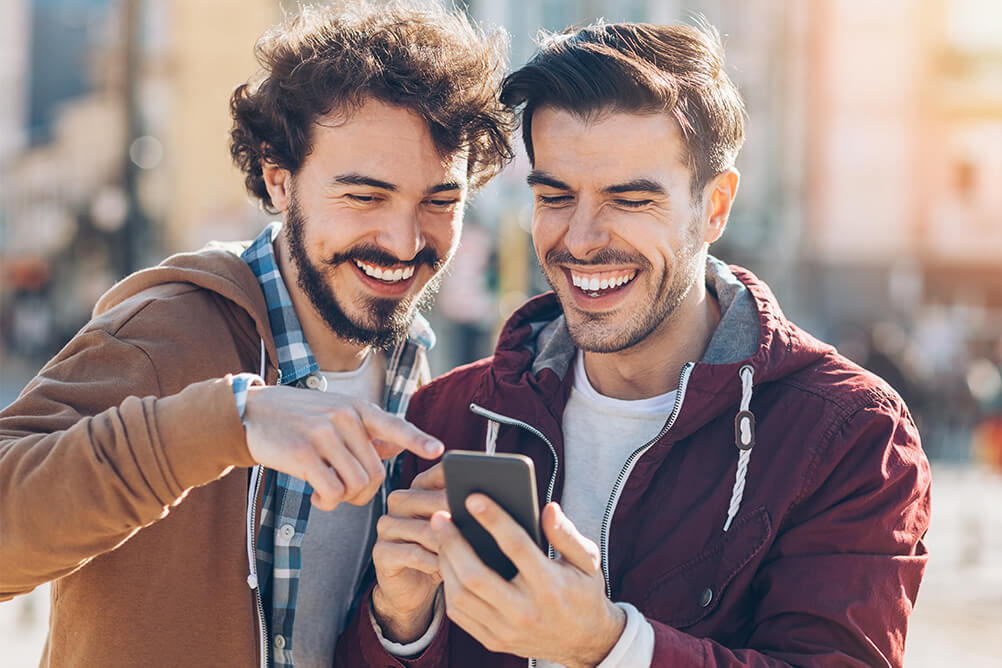 Zwei Freunde lachen über verrückte Lottogeschichten, die sie auf einem Smartphone lesen
